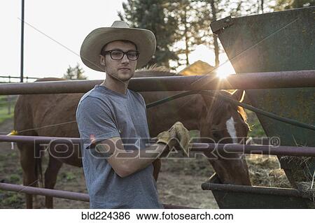 Stock Photograph - Caucasian farmer leaning on railing near horse. Fotosearch