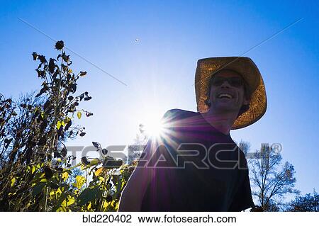 Stock Image - Caucasian farmer wearing straw hat under blue sky. Fotosearch
