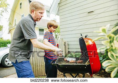 Caucasian father and son grilling food in backyard View Large Photo Image Stock Photo - Caucasian father and son grilling food in backyard. Fotosearch