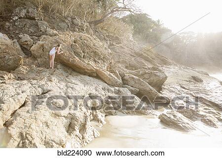 Stock Image - Caucasian girl climbing rocks at beach. Fotosearch