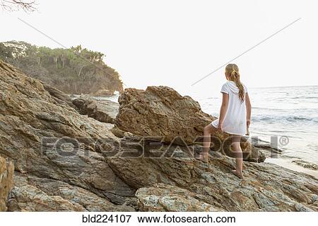 Stock Photo - Caucasian girl climbing rocks at beach. Fotosearch