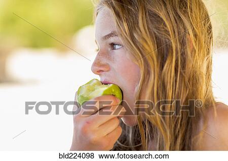 Stock Photo - Caucasian girl eating green apple. Fotosearch