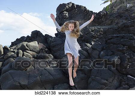 Stock Photo - Caucasian girl jumping off rocks at beach. Fotosearch