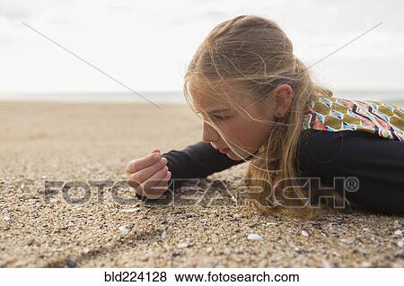 Caucasian girl laying on beach examining seashells View Large Photo Image Stock Photo - Caucasian girl laying on beach examining seashells. Fotosearch