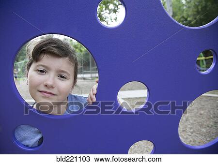Stock Image - Caucasian girl peeking through play structure. Fotosearch