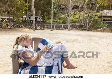Stock Photo - Caucasian girl sitting in beach chair playing game. Fotosearch