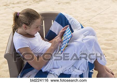 Stock Photograph - Caucasian girl sitting in beach chair playing game. Fotosearch