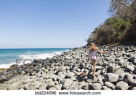 Stock Photograph - Caucasian girl walking on rocks at beach. Fotosearch
