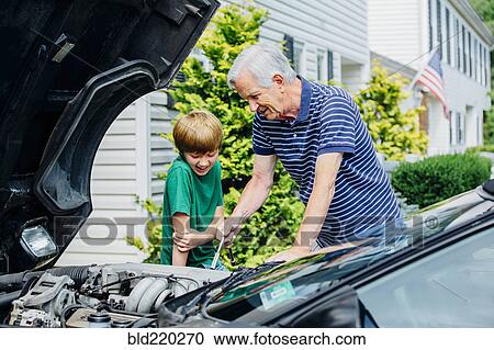 Stock Image - Caucasian grandfather and grandson working on car in driveway. Fotosearch