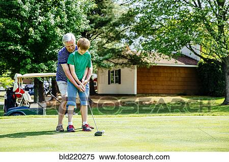 Stock Photography - Caucasian grandfather teaching grandson golf on course. Fotosearch