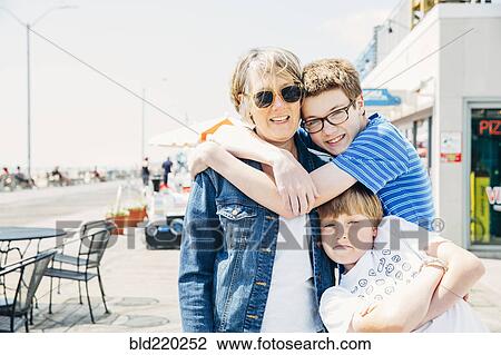Stock Image - Caucasian grandmother and grandsons hugging in city. Fotosearch