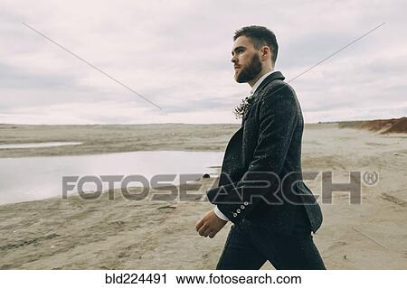 Stock Image - Caucasian groom walking on beach. Fotosearch