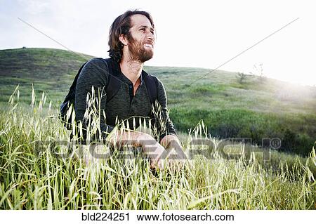 Stock Image - Caucasian hiker crouching in grass on mountain. Fotosearch