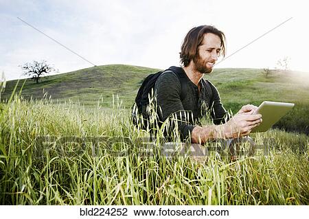 Caucasian hiker crouching in grass on mountain using digital tablet View Large Photo Image Stock Image - Caucasian hiker crouching in grass on mountain using digital tablet. Fotosearch