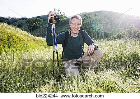 Picture - Caucasian hiker kneeling in grass on mountain. Fotosearch
