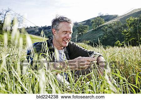 Stock Photo - Caucasian hiker sitting in tall grass using cell phone. Fotosearch