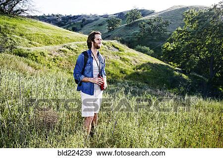 Stock Photo - Caucasian hiker standing in grass on mountain holding water bottle. Fotosearch