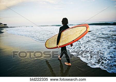 Stock Photography - Caucasian man carrying surfboard at beach. Fotosearch