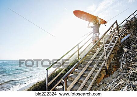 Picture - Caucasian man carrying surfboard on stairs at beach. Fotosearch