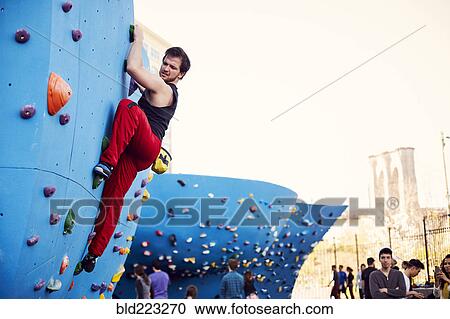 Stock Image - Caucasian man climbing outdoor climbing wall. Fotosearch