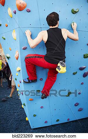 Stock Photo - Caucasian man climbing outdoor climbing wall. Fotosearch