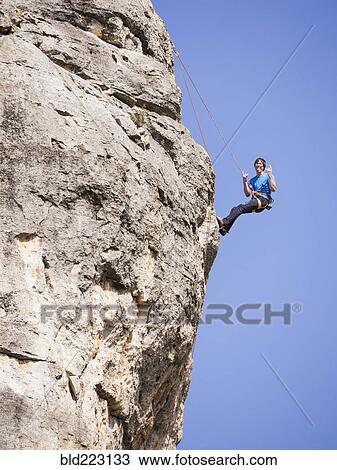 Stock Image - Caucasian man climbing rock gesturing with tongue out. Fotosearch