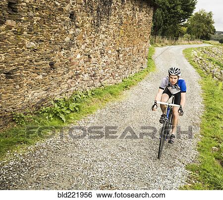 Stock Photograph - Caucasian man cycling on gravel path. Fotosearch