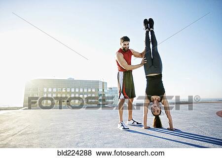 Stock Photo - Caucasian man helping woman do handstand on urban rooftop. Fotosearch