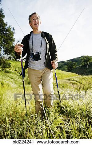 Stock Image - Caucasian man hiking in grass on mountain. Fotosearch