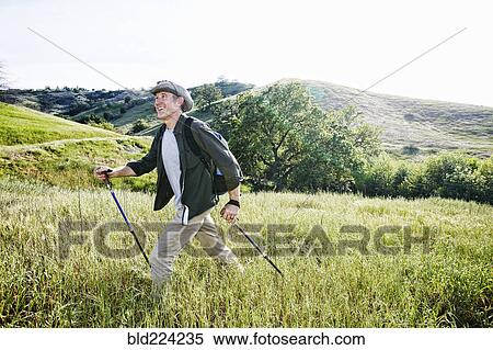 Stock Photography - Caucasian man hiking in grass on mountain. Fotosearch