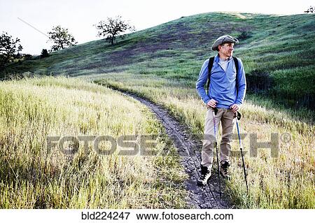 Stock Photo - Caucasian man hiking on dirt path on mountain. Fotosearch