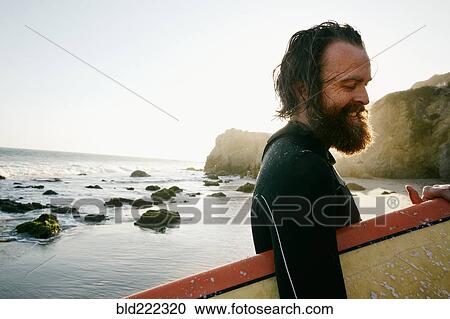 Caucasian man holding surfboard at beach View Large Photo Image Stock Image - Caucasian man holding surfboard at beach. Fotosearch
