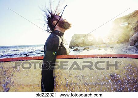 Stock Image - Caucasian man holding surfboard at beach. Fotosearch