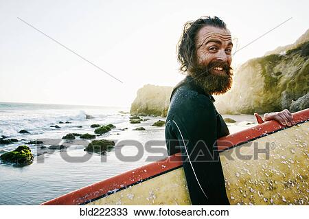 Stock Image - Caucasian man holding surfboard at beach. Fotosearch