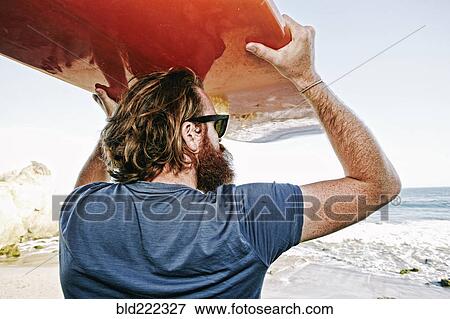 Stock Photo - Caucasian man holding surfboard at beach. Fotosearch