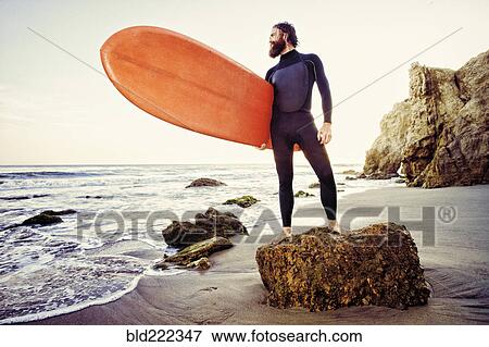 Stock Photo - Caucasian man holding surfboard at beach. Fotosearch