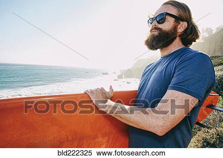 Stock Photography - Caucasian man holding surfboard at beach. Fotosearch