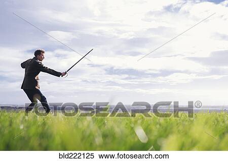 Stock Photography - Caucasian man holding sword in field. Fotosearch
