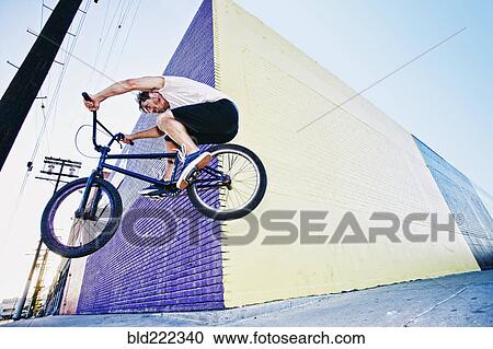 Stock Image - Caucasian man jumping on BMX bike on sidewalk. Fotosearch