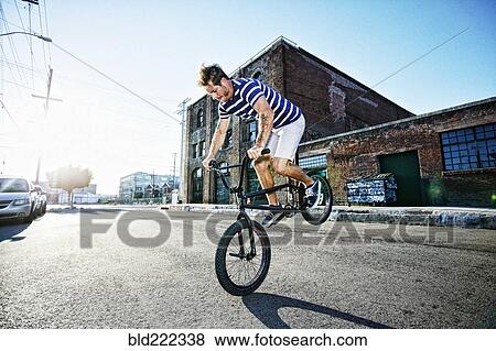 Stock Photo - Caucasian man riding BMX bike on street. Fotosearch