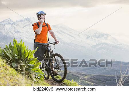 Stock Image - Caucasian man riding mountain bike resting and drinking water. Fotosearch