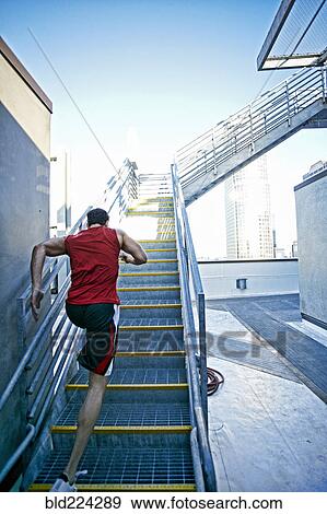 Stock Photo - Caucasian man running up staircase on urban rooftop. Fotosearch