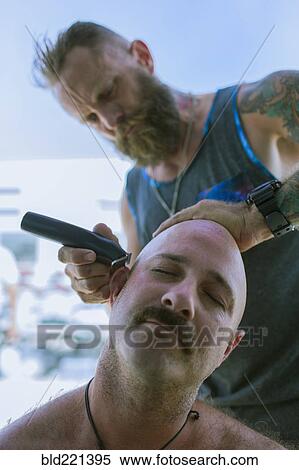 Stock Photography - Caucasian man shaving head of friend. Fotosearch