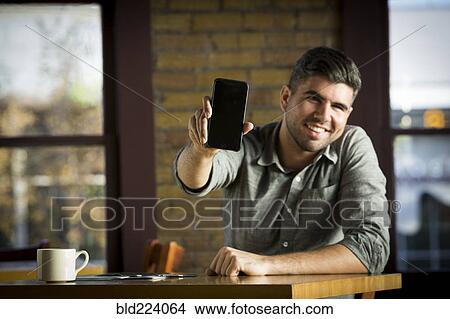 Picture - Caucasian man showing cell phone in cafe. Fotosearch