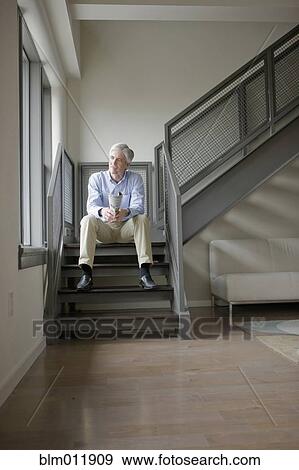 Stock Photo - Caucasian man sitting in modern staircase. Fotosearch