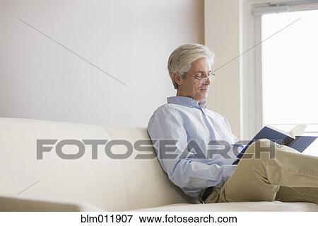 Stock Photo - Caucasian man sitting on sofa reading book. Fotosearch