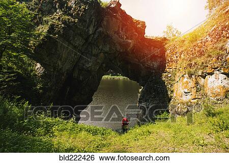 Stock Photograph - Caucasian man under rock formation arch. Fotosearch