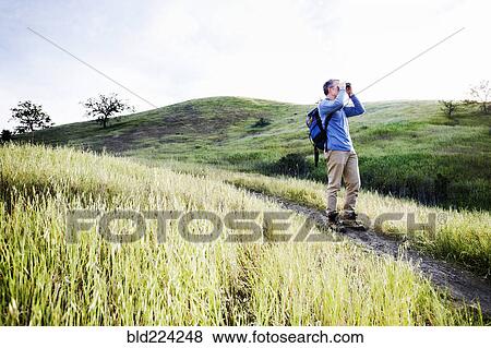 Stock Photo - Caucasian man using binoculars on dirt path. Fotosearch