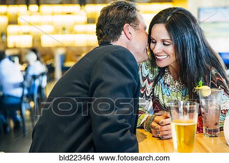 Picture - Caucasian man whispering to ear of woman in restaurant. Fotosearch