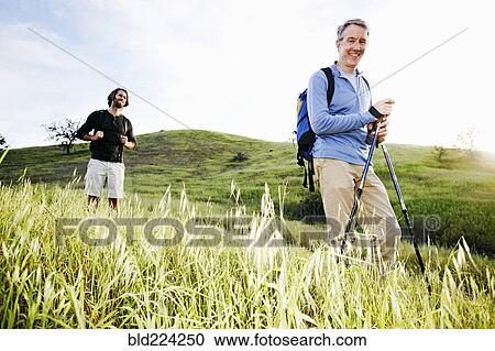 Stock Image - Caucasian men hiking in grass on mountain. Fotosearch